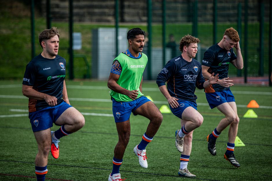 Four rugby players warming up during a practice session on an artificial grass field in Birmingham.