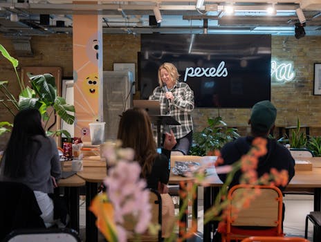 A woman leading a workshop in a stylish office setting, engaging with a small audience.