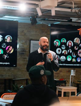 Speaker presenting in a modern office with digital screens displaying a team project.