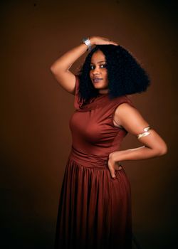 Confident woman in brown dress strikes a graceful pose against a warm backdrop.