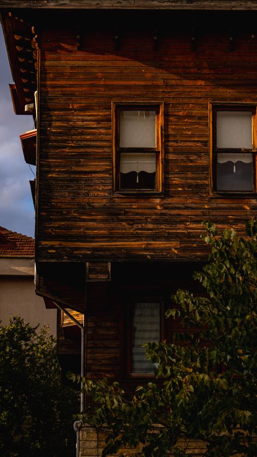 Free A rustic wooden house facade illuminated by soft natural light, surrounded by greenery. Stock Photo