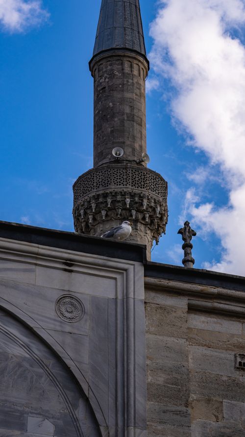 Free A stone minaret with intricate carvings and a bird perched below against a blue sky. Stock Photo