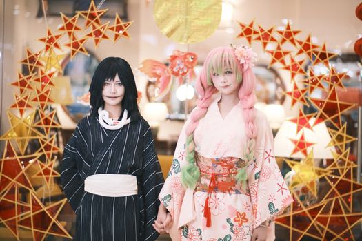 Two cosplayers in vibrant kimonos at an indoor Japanese-themed event with star decor.