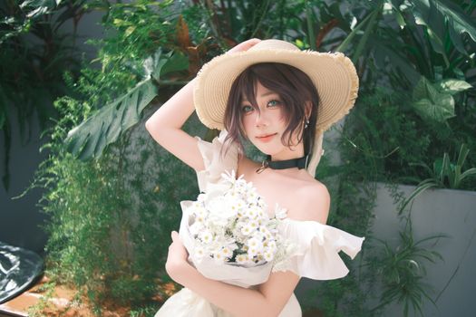 A woman in a straw hat holds a bouquet of daisies in a lush garden setting.
