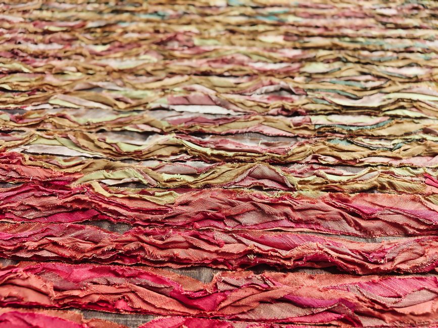 Close-up view of a colorful, textured fabric surface with layers of vibrant reds and browns.