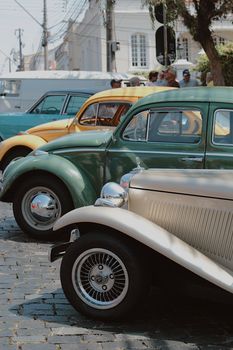 Classic vintage cars showcased on a sunny street in Curitiba, Brazil.