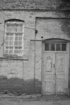 Black and white photo of a vintage brick wall featuring an old wooden door and window.