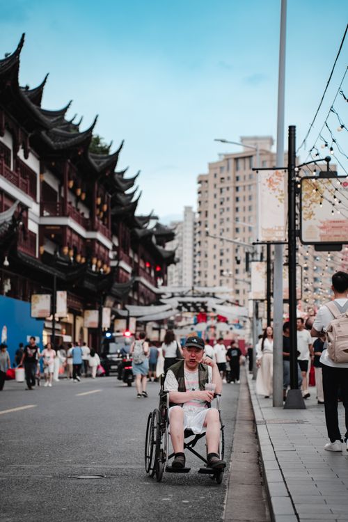 Free Crowded Asian street scene with a person in a wheelchair, traditional architecture, and city backdrop. Stock Photo