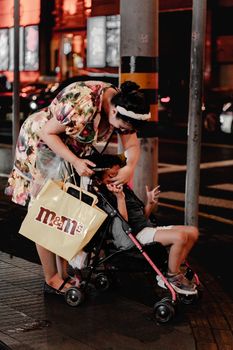 A mother tending to her child in a stroller at night on a city street.