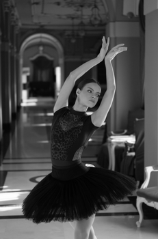 Black and white photo of a ballerina striking a poised pose inside an ornate hallway.