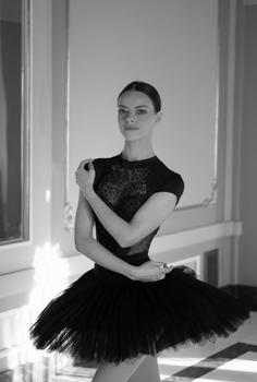 Black and white photo of a graceful ballerina posing elegantly indoors.
