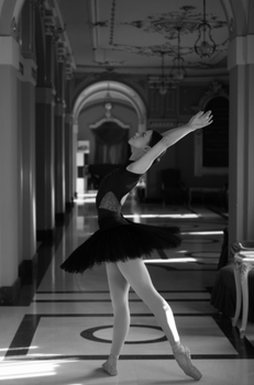 Elegant black and white photo of a ballerina in a pose within a classical hallway setting.