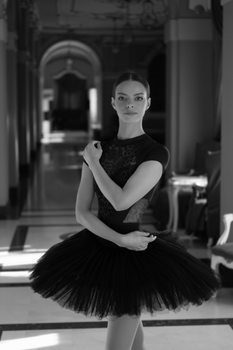 Ballet dancer gracefully posing in a historic, elegant hallway, captured in black and white.