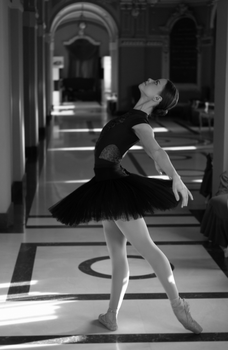 Black and white photo of a graceful ballet dancer in a classic arched corridor.