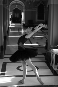 Black and white photo of a ballerina dancing in a grand hallway, embodying grace and poise.