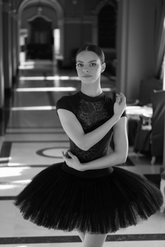 Ballerina posing gracefully in a black tutu inside a stylish hall, embodying elegance and poise.