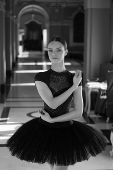 Black and white portrait of a poised ballerina in a hallway, showcasing elegance and grace.