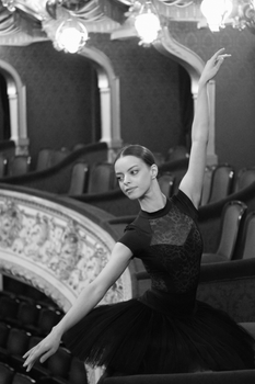 Graceful ballet dancer posing in a theater balcony, captured in black and white.