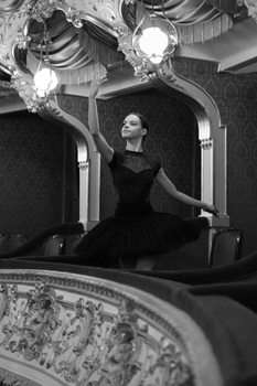 Black and white portrait of a ballerina poised in a luxurious theater setting.