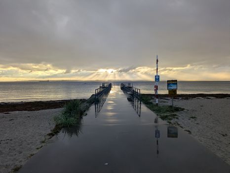 Peaceful scene of a pier extending into the ocean during sunset with dramatic clouds.