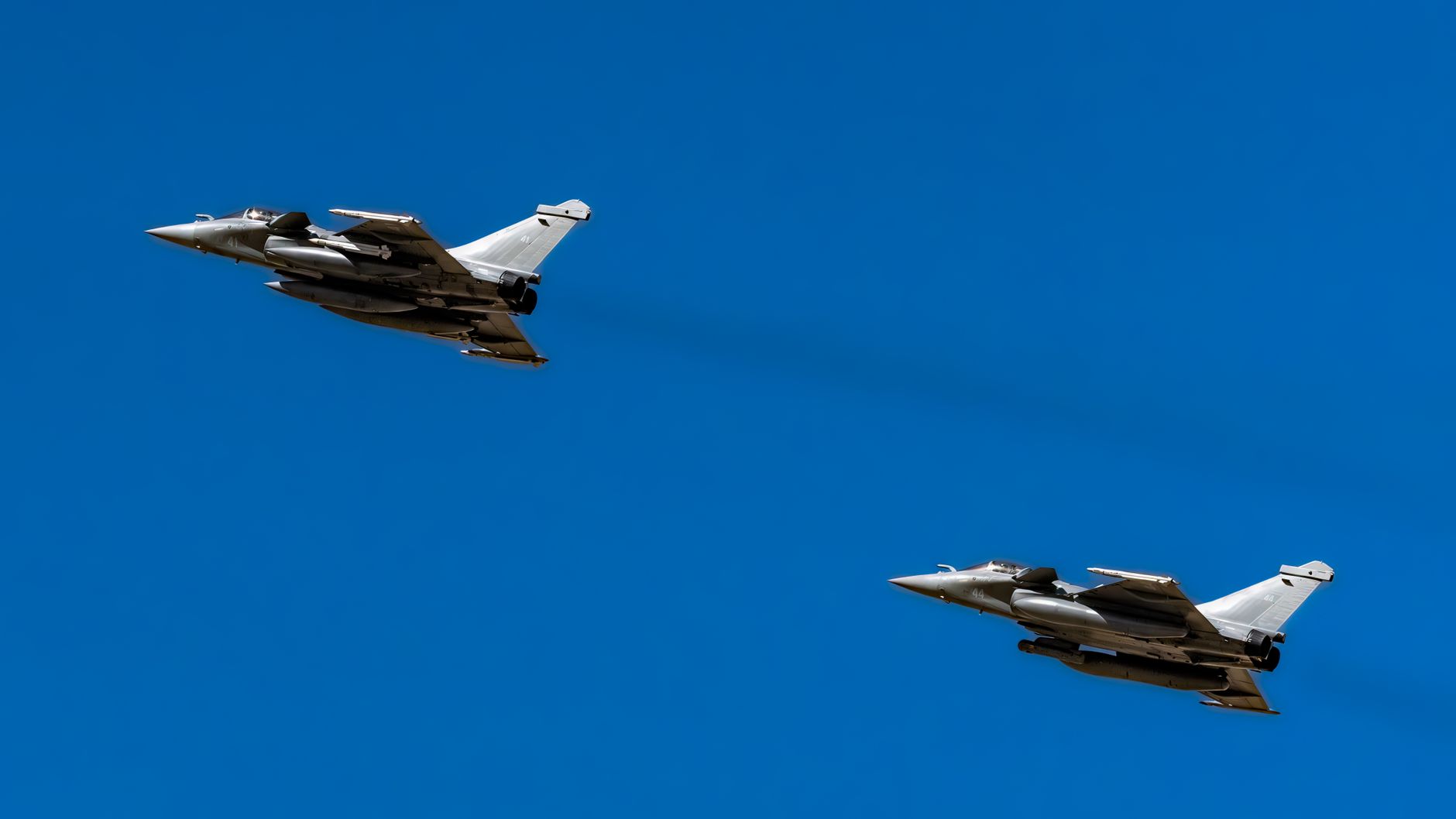 Two Rafale jets soar through a clear blue sky over Los Llanos, Spain.
