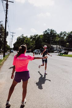A volunteer assists a marathon runner by passing water during an outdoor event on a sunny day.