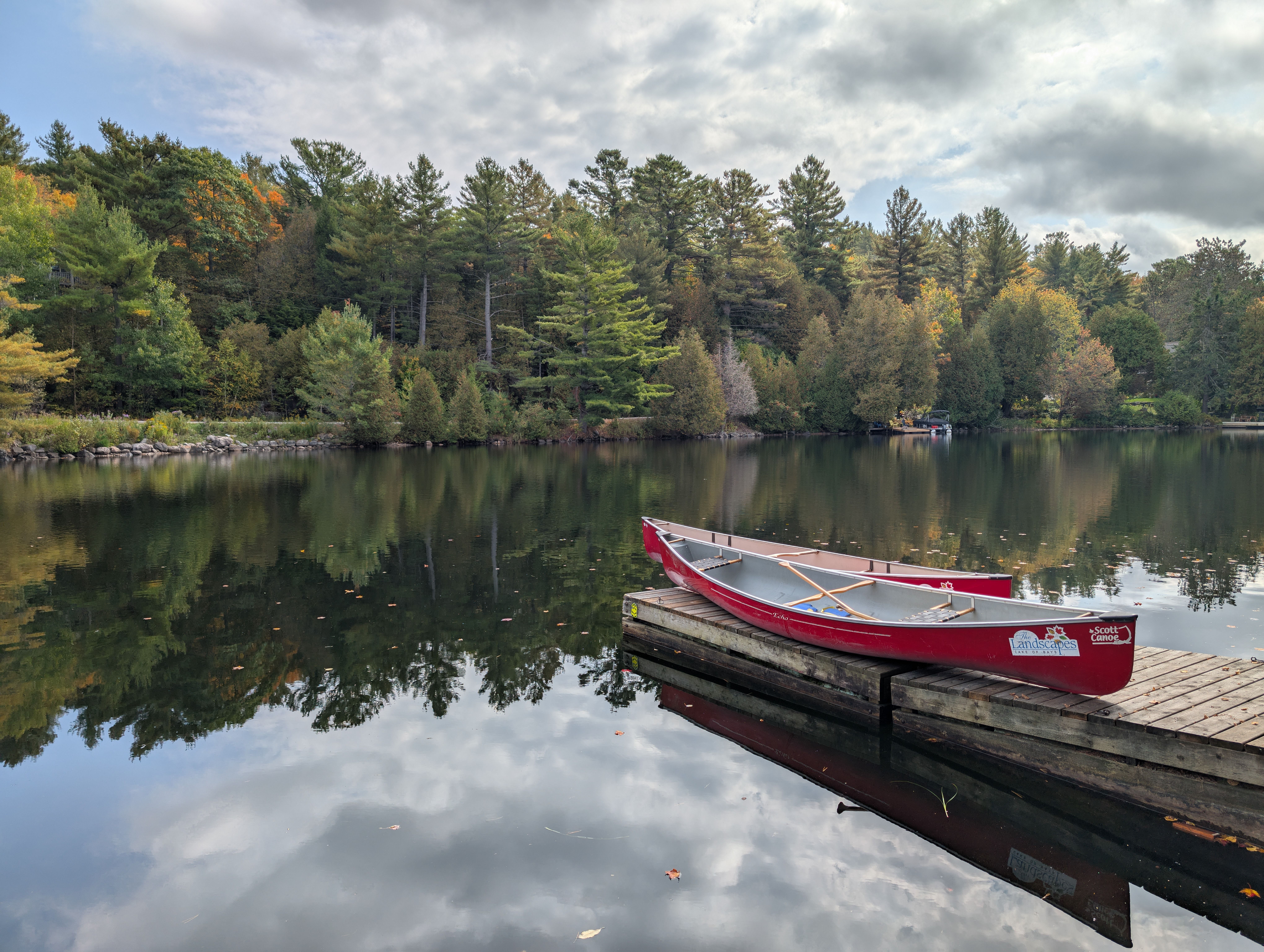 A tranquil scene of a red canoe on a dock by a reflective lake surrounded by lush forest.