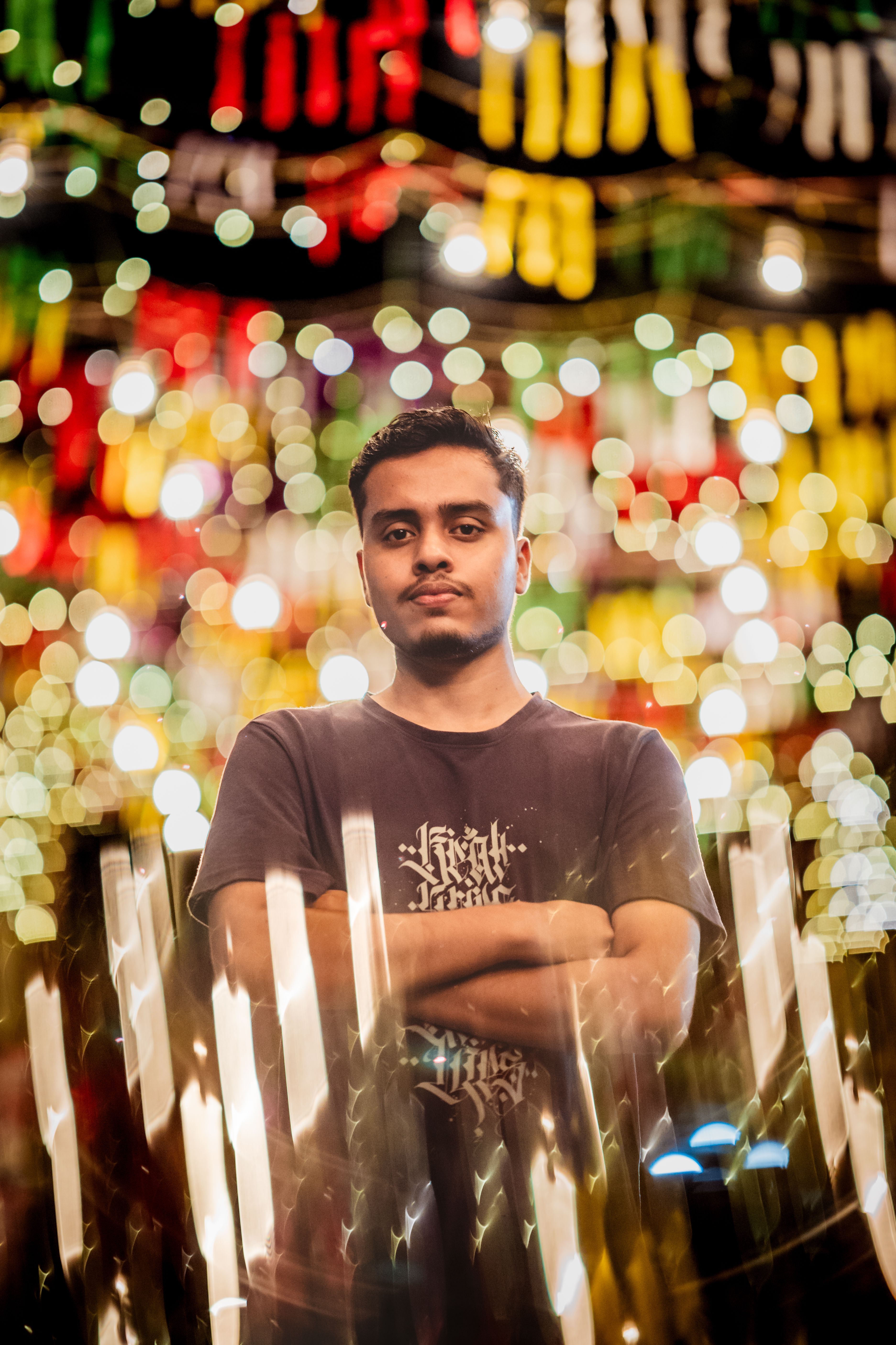 A young man stands confidently with colorful festival lights in Dhaka, Bangladesh. Vibrant night scene.