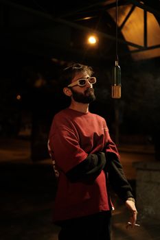 A young man with sunglasses poses under a streetlight, creating a moody nighttime atmosphere.