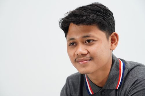 Free A close-up portrait of a young man smiling, wearing a gray polo shirt with a white background. Stock Photo