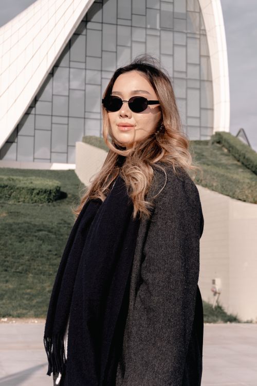 Free Fashionable woman with sunglasses poses outdoors near modern architectural structure on a sunny day. Stock Photo