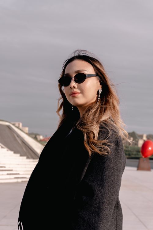 Free Fashionable adult woman in sunglasses posing confidently outdoors with a contemporary background. Stock Photo
