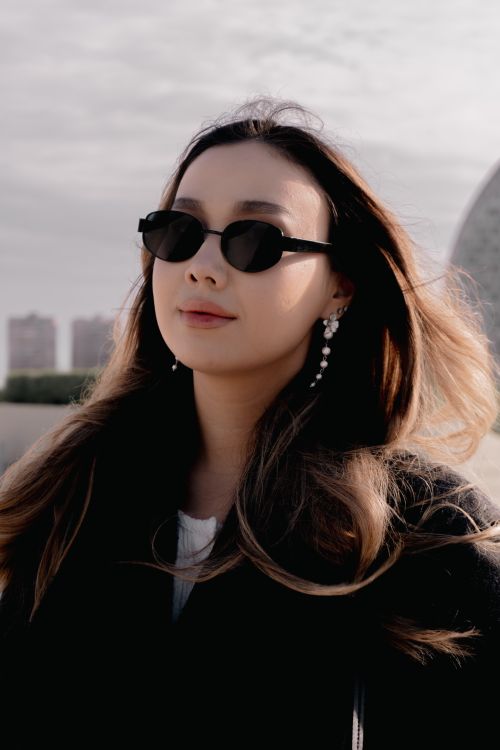 Free A fashionable woman wearing sunglasses and earrings stands outdoors in daylight. Stock Photo