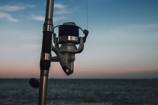 Close-up of a fishing rod by the ocean during sunset, capturing serene aquatic leisure.