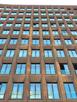 A multi-story brick building with reflective windows viewed from below.