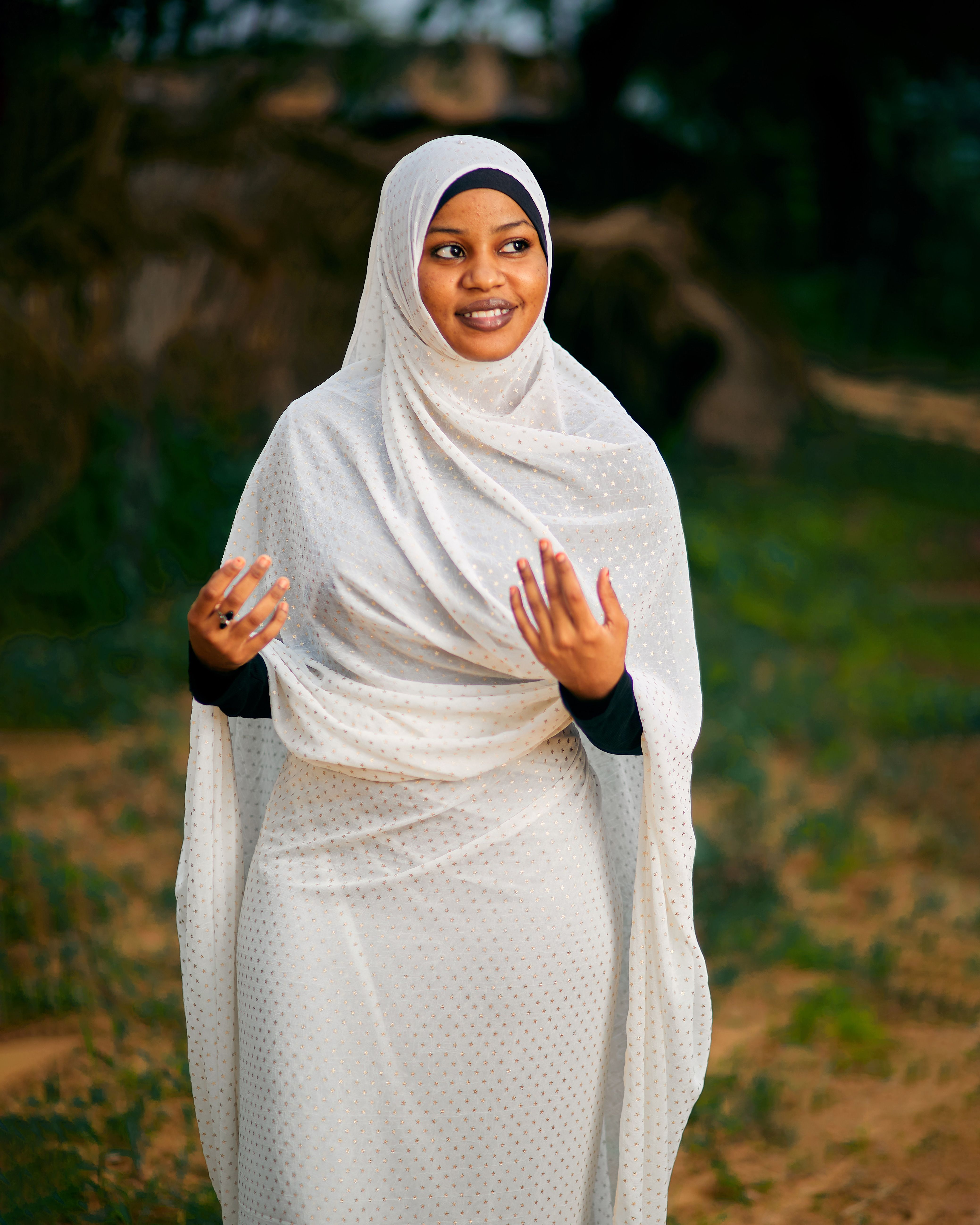 A joyful woman wearing a white hijab stands outdoors, expressing happiness.
