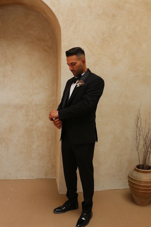 Free A man in a tuxedo adjusts his watch in a stylish indoor setting. Stock Photo