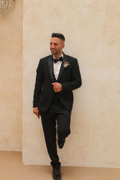 Free A handsome man in a black tuxedo with a boutonniere, posing elegantly indoors. Stock Photo
