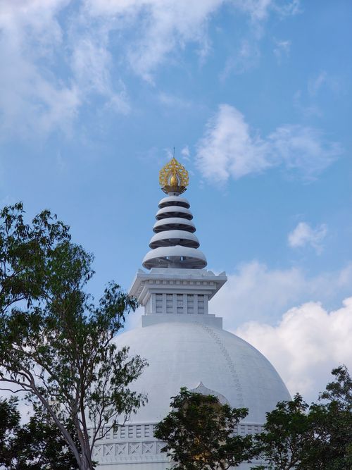 Free White stupa against a clear blue sky surrounded by trees. Serene and architectural beauty. Stock Photo