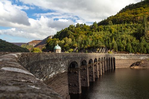 Free A picturesque dam surrounded by lush forests in Wales under a vibrant sky. Stock Photo
