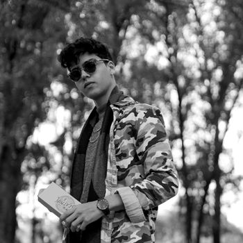 Black and white photo of a fashionable young man outdoors in sunglasses and a camouflage jacket.