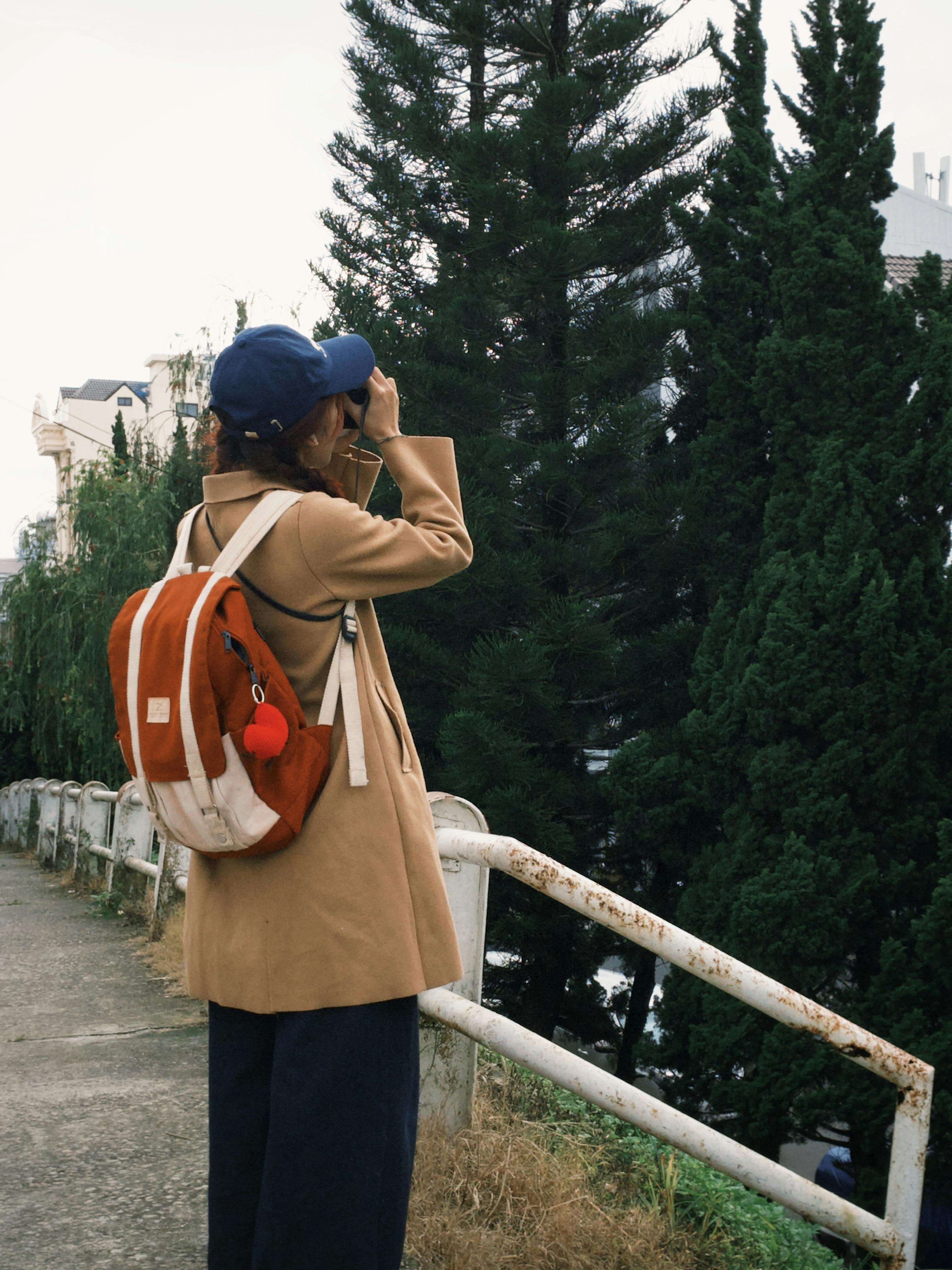 Woman in a coat and cap with a backpack exploring an outdoor path.