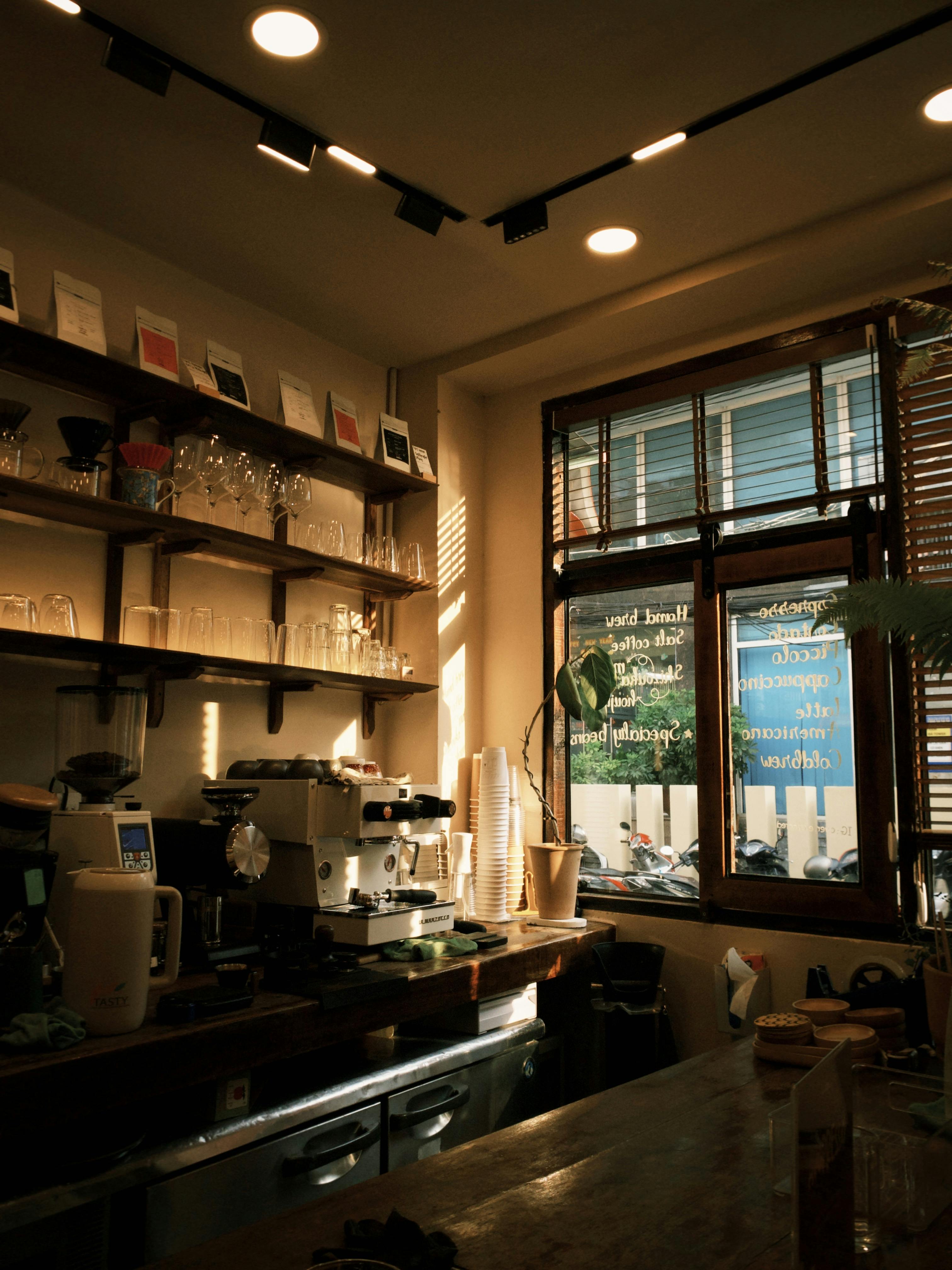 Warm sunlight casts a cozy glow inside an artisan coffee shop with shelves of glassware.