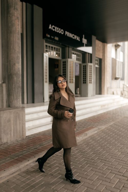 Free Stylish woman walking past a building entrance, holding a coffee cup. Stock Photo