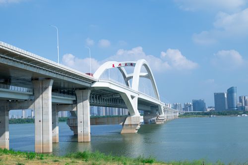 Free A modern arch bridge spanning a river against a city skyline with clear blue skies. Stock Photo