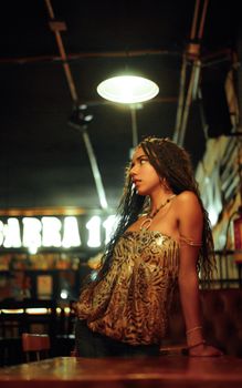 Portrait of a stylish woman leaning on a table in a dimly lit, trendy bar setting, exuding a modern and fashionable vibe.
