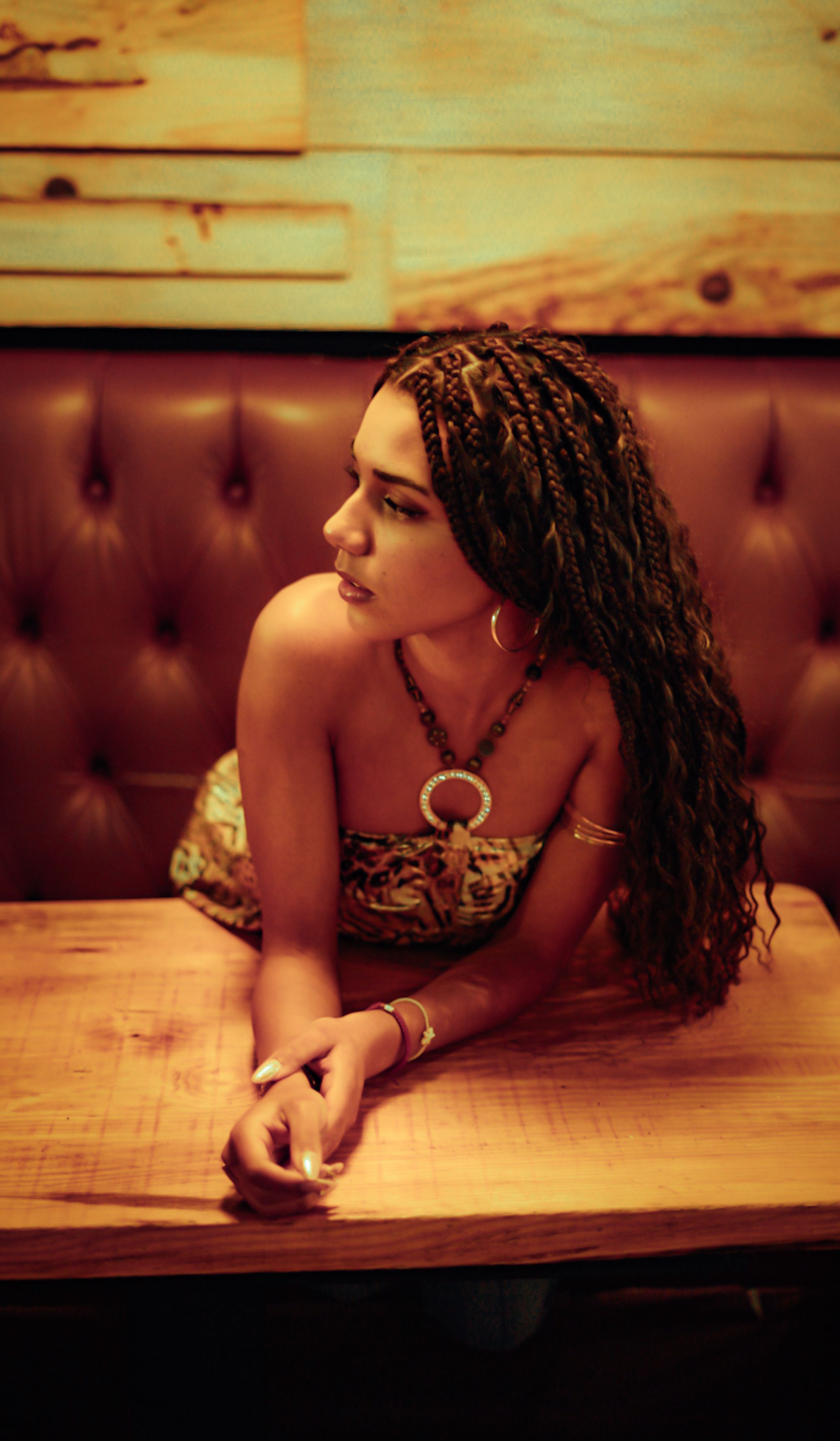 Stylish woman with braided hair poses at a wooden table in a cozy cafe, creating a warm and inviting atmosphere.