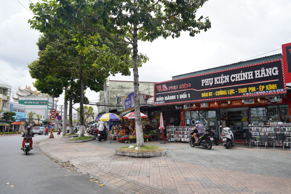 Lively shopping street in Mong Cai with colorful storefronts, fashion items, electronics, local shoppers, bilingual signs, energetic summer urban scene, highly detailed