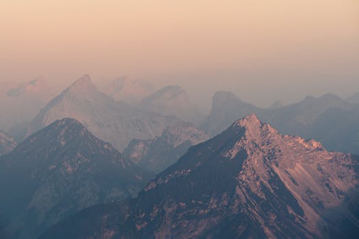 Scenic view of sunlit alpine peaks enveloped in a pastel sky at sunrise.