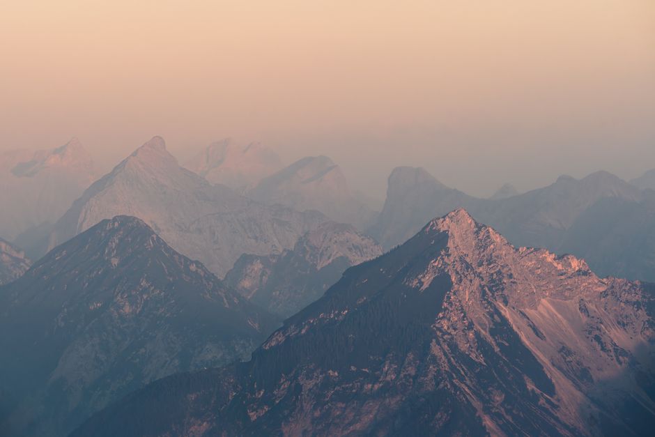 Scenic view of sunlit alpine peaks enveloped in a pastel sky at sunrise.